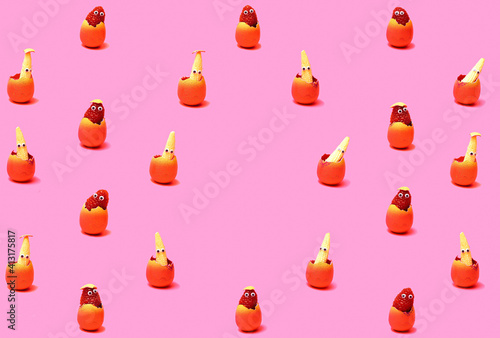 Pattern created of raspberry and baby corns with wiggle eyes in pink egg shell with egg shells on the bottom. Egg shaped copy space in the middle. Pink background.