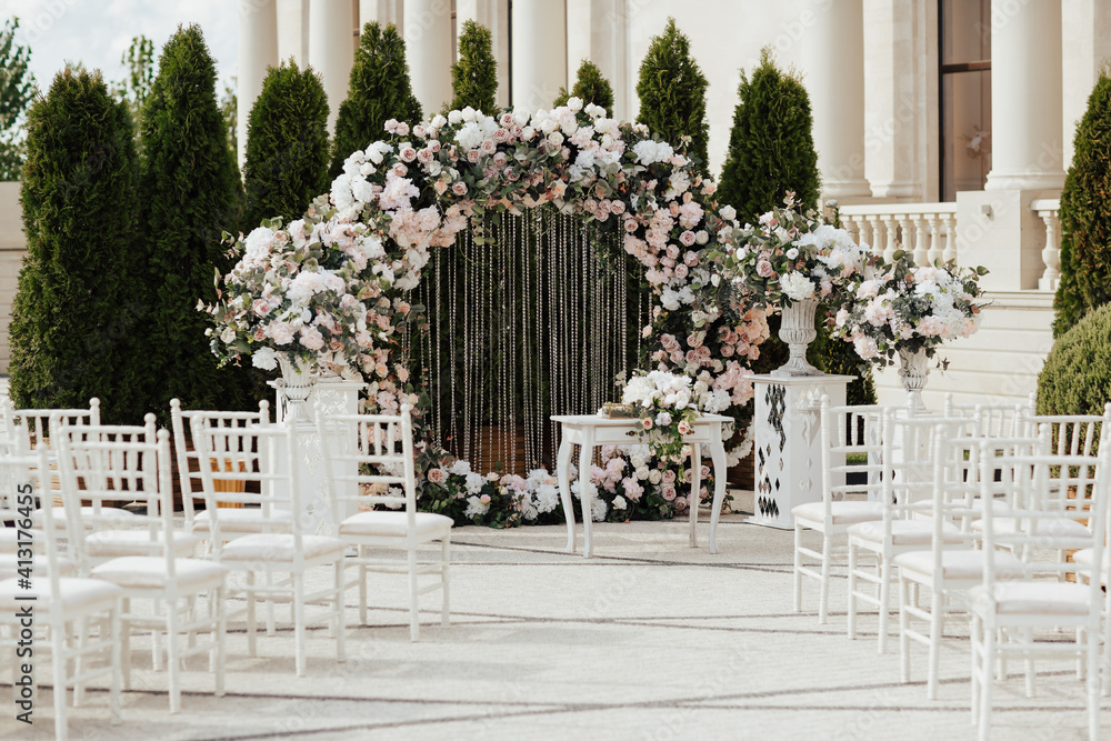 Beautiful modern round wedding arch for unique luxury wedding ceremony with fresh flowers. White chairs near.