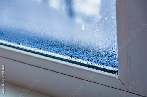 A fragment of a plastic window with condensation of water on the glass. Concept: defective plastic window with condensation, temperature difference, cooling, humidity in the room. photo