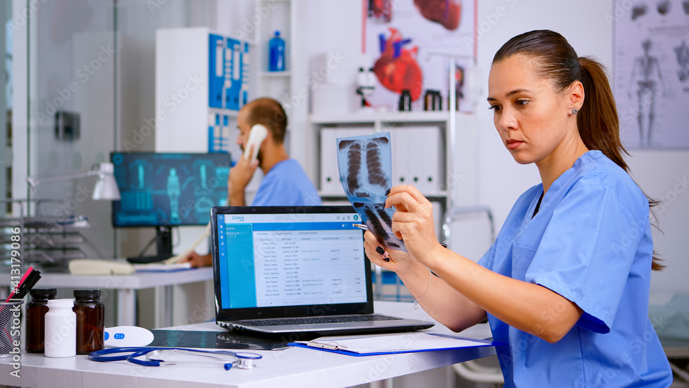 Medical doctor nurse holding and analysing radiography checking treatment of diagnosed patients, writing informations in laptop. Assistant working in hospital making appointments and registration. Medical doctor nurse holding and analysing radiography checking treatment of diagnosed patients, writing informations in laptop. Assistant working in hospital making appointments and registration.