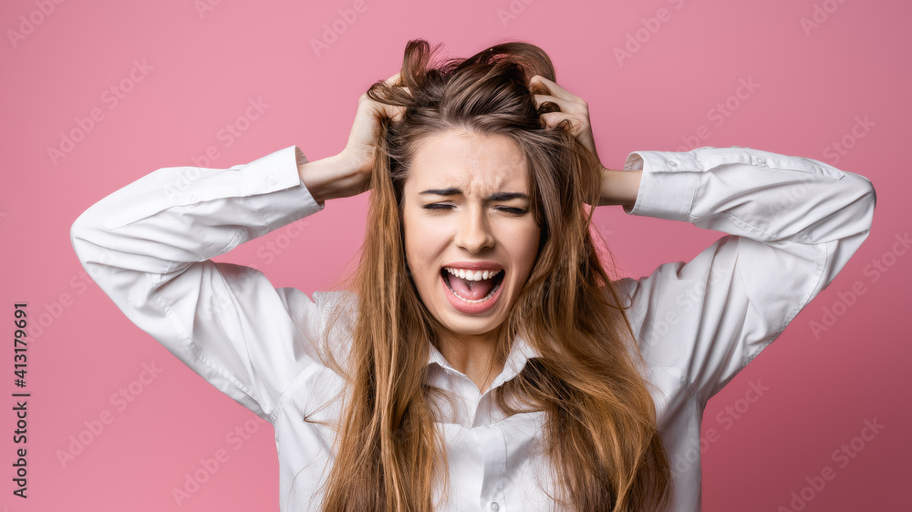 Portrait of woman in panic shouting and grabbing her head in fear or frustration. Studio shot, pink background Portrait of woman in panic shouting and grabbing her head in fear or frustration. Studio shot, pink background