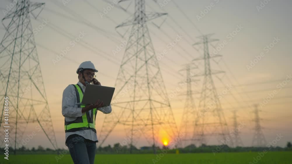 An electrical engineer with a laptop talking on the phone High voltage tower inspection report before starting a project Assigned by the organization during the time of sunset or sunrise. An electrical engineer with a laptop talking on the phone High voltage tower inspection report before starting a project Assigned by the organization during the time of sunset or sunrise.