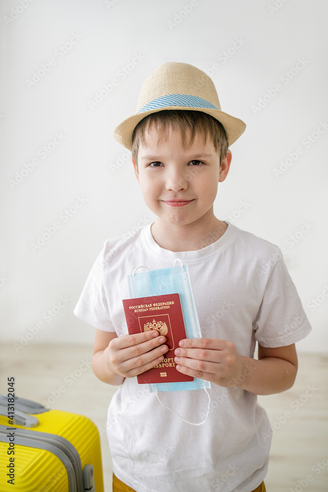 The child smiles and holds a international passport and a medical mask in his hands. The child smiles and holds a international passport and a medical mask in his hands.