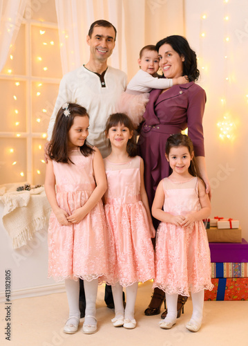 family portrait of a parents and children in home interior decorated with lights and holiday gifts
