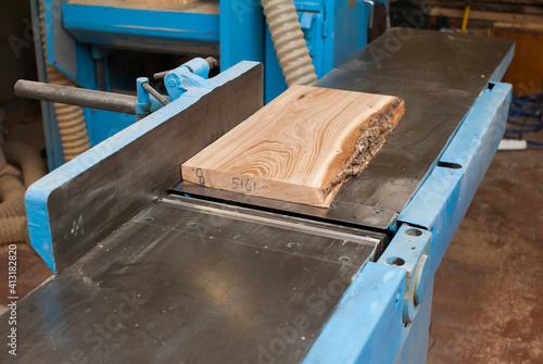a rough board lies on a large jointer in a carpentry shop. Manufacturing of wooden furniture photo