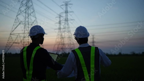 Two electrical engineers discussing a project on a high-voltage tower in the evening.