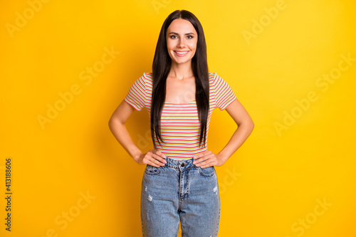 Photo portrait of young woman smiling keeping hands on waist in casual clothes isolated on bright yellow color background