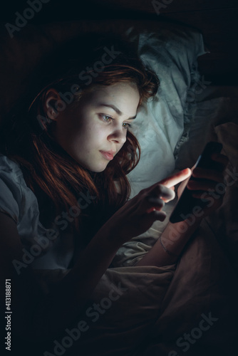 woman in the room lies in bed with a phone in her hands addiction
