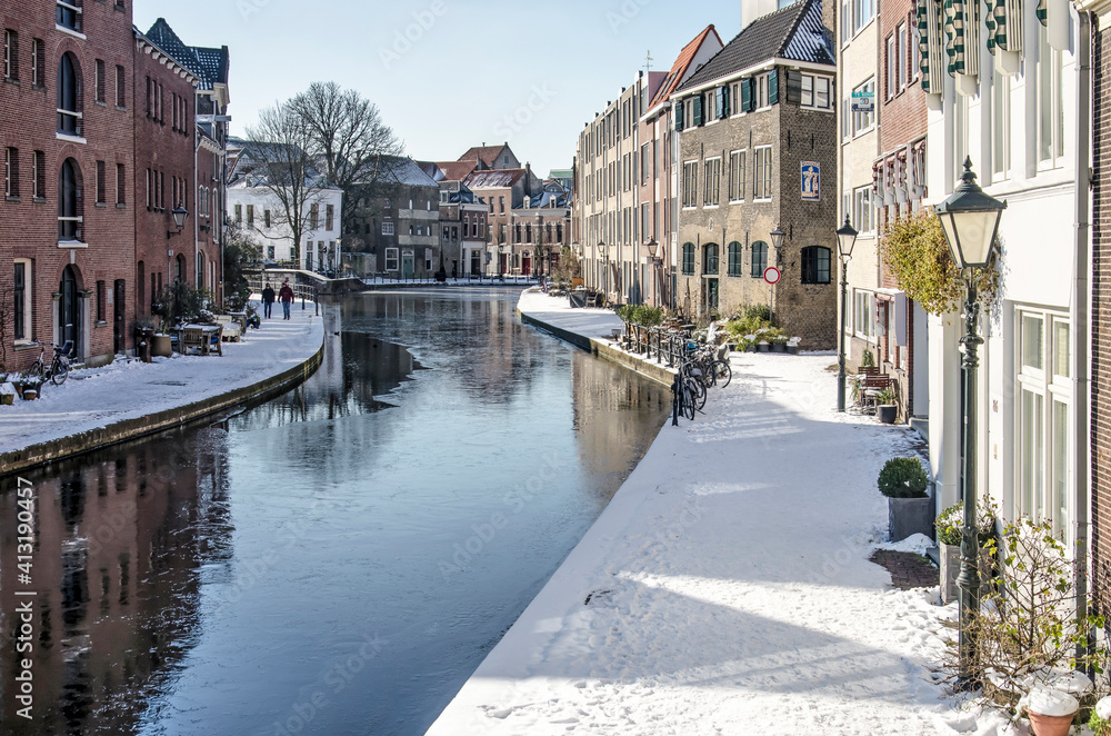 Schiedam, The Netherlands, February 11, 2021: View along the frozen river Schie lined with snow-covered quays and historic brick and plaster houses