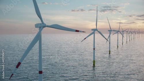 Camera pulls back to show an aerial view of a long row of offshore wind turbines in the sea against low sun. Green and renewable energy concept. Realistic high quality 3d animation. 
