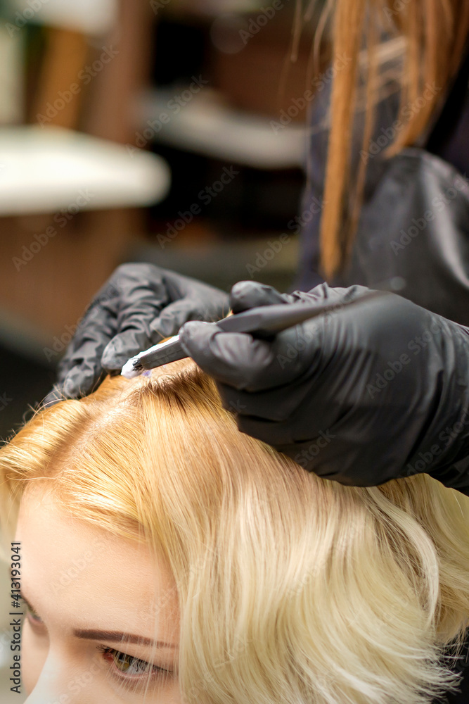 Fototapeta premium A closeup head of a young blonde woman receiving dyeing hair in a hair salon