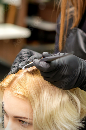 A closeup head of a young blonde woman receiving dyeing hair in a hair salon