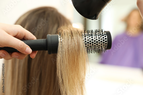 Stylist drying client's hair in beauty salon, closeup