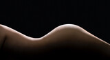 Female body curves in dark. Sexy shape and figure of a beautiful nude woman. Slim waist and perfect skin. Hot erotic naked model. Side torso, hips and buttocks. Low key silhouette on black background.