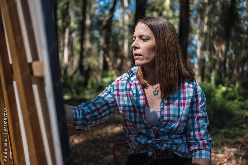 Fototapeta premium Young woman painting the landscape outdoors.