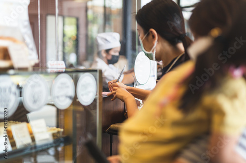 Woman customer in protective mask signing on receipt at counter in cafe