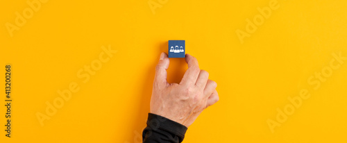 Male hand holds a blue wooden cube with team icon on yellow background.