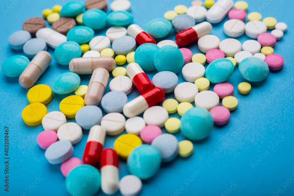 A lot of multicolored pills and capsules on a blue background as a concept of addiction from medicine. Vitamins to keep immunity on a high level. A lot of multicolored pills and capsules on a blue background as a concept of addiction from medicine. Vitamins to keep immunity on a high level.