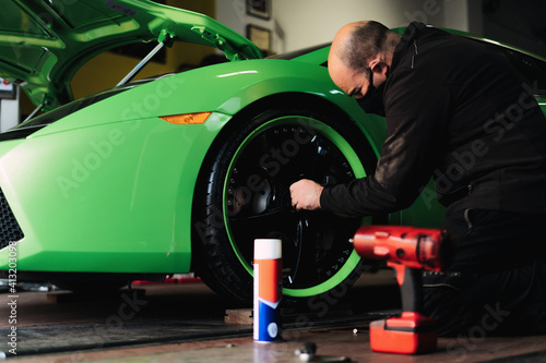 Mechanic changing the wheels of a high-end super sports car. Auto mechanic working in garage. Repair service.