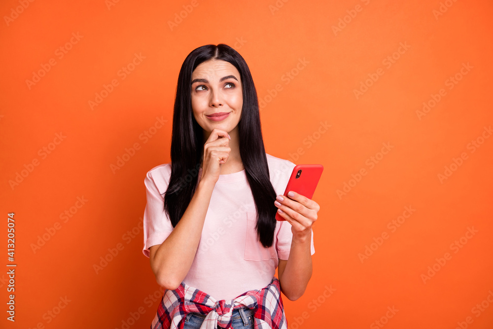 Portrait of charming positive girl arm on chin look interested empty space isolated on orange color background Portrait of charming positive girl arm on chin look interested empty space isolated on orange color background