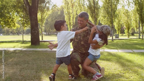 Happy military dad wearing uniform, coming home after mission, meeting children outdoors, hugging kids. Family reunion concept