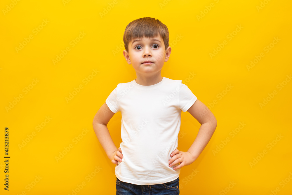 Happy child in a white t-shirt holds his hands on the belt on an isolated yellow background Happy child in a white t-shirt holds his hands on the belt on an isolated yellow background