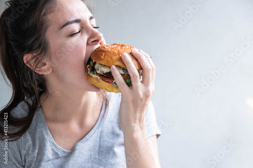 Close up portrait of a hungry young woman eating burger over white background
