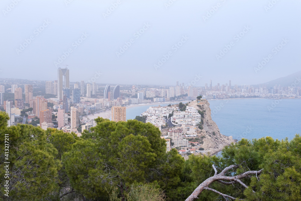 Elevated panoramic view of a large city with skyscrapers on the Mediterranean Sea with pine trees in the foreground.