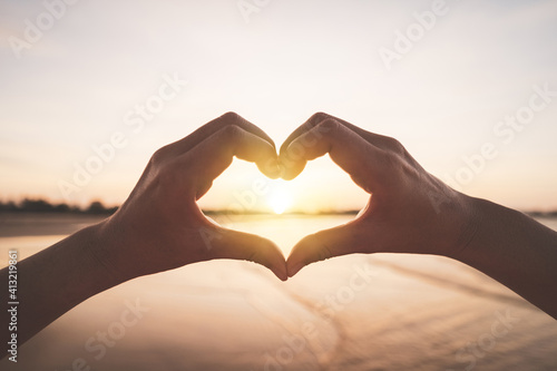 Female hands heart shape on nature bokeh sun light flare wave and blur tropical beach abstract background.