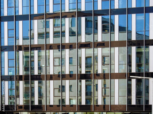 Reflection of a multi-storey apartment building in the large glass window walls of a modern office construction 