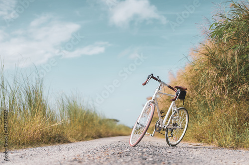 Fototapeta Naklejka Na Ścianę i Meble -  Vintage bicycle on country road and field with blue sky and white cloud abstract background.