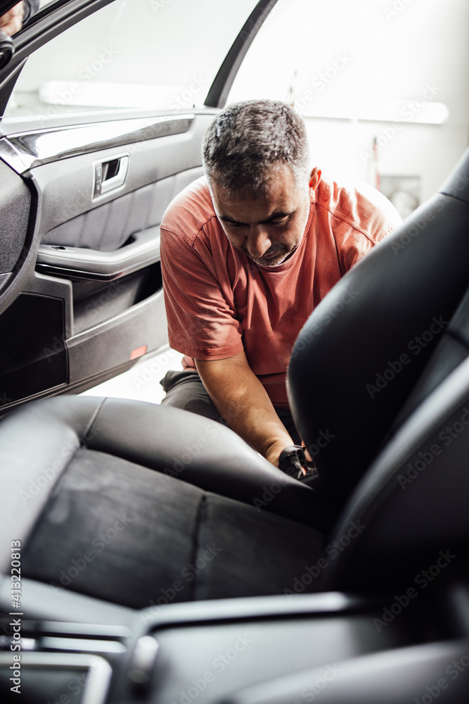 Car wash service worker wet cleaning vehicle interior and seats. Old car restoration work. Car wash service worker wet cleaning vehicle interior and seats. Old car restoration work.