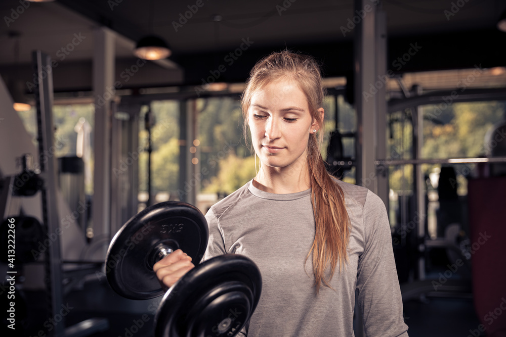 Obraz premium famle athlete is doing a workout with a heavy dumbbell in a gym