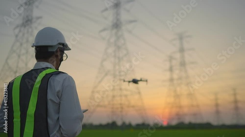 An electrical engineer forcing a drone To inspect high voltage poles before starting a project Assigned by the organization during the sunset time

