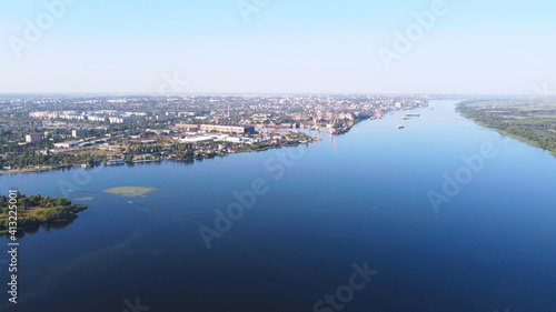 Drone fly over waving river of blue color surrounded by local village with various buildings and Wetland and marsh habitat with a reedbed of Common Reed aerial view. © nata_zhekova