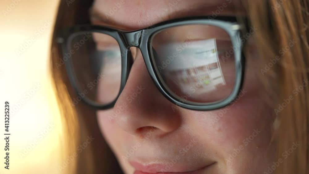 Woman in glasses looking on the monitor and surfing Internet. The monitor screen is reflected in the glasses. Work at night. Home Office. Remote work Woman in glasses looking on the monitor and surfing Internet. The monitor screen is reflected in the glasses. Work at night. Home Office. Remote work
