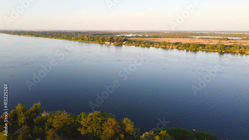 Drone fly over waving river of blue color surrounded by local village with various buildings and Wetland and marsh habitat with a reedbed of Common Reed aerial view. © nata_zhekova