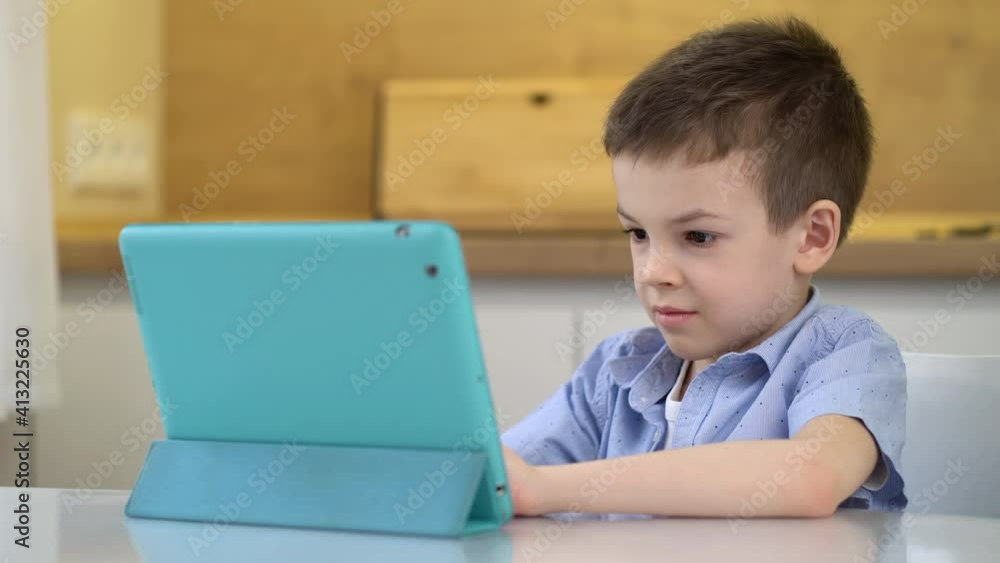 Preschooler sits at a table and looks at a digital tablet. Preschooler sits at a table and looks at a digital tablet.