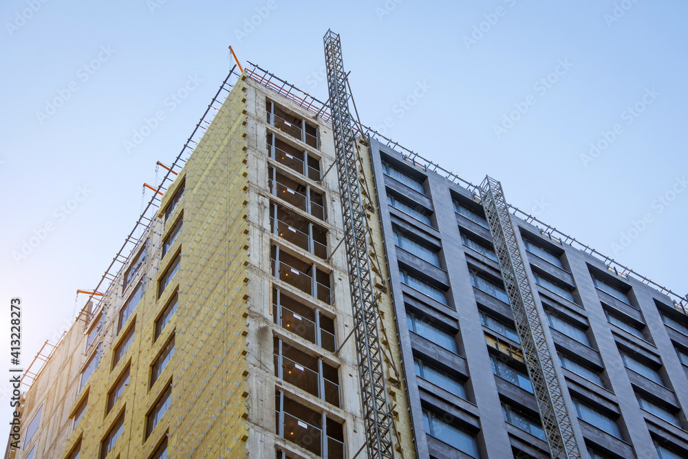 Corner of a multi-storey building under construction and a construction elevator rail outside the building to lift workers. Corner of a multi-storey building under construction and a construction elevator rail outside the building to lift workers.