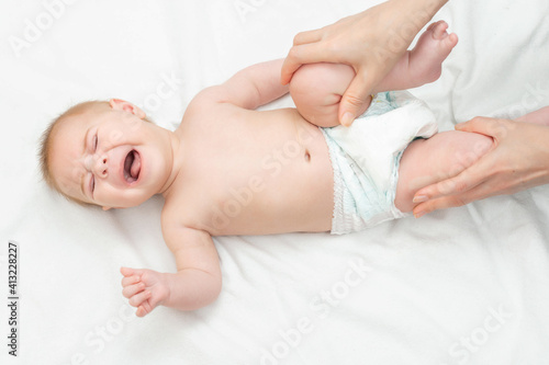 The masseur gives a gymnastic to the newborn baby. Massage for children relieving tone. Three month old baby crying doing gymnastics