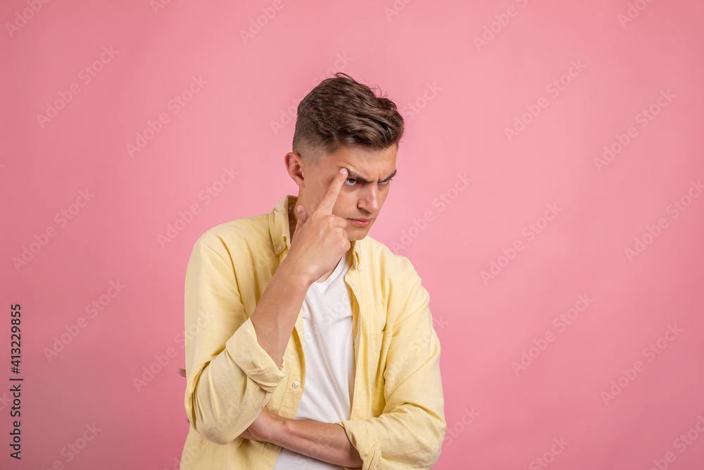 Young man thinking . Handsome man in casual clothes is pointing away, looking at camera and smiling, on pink background Young man thinking . Handsome man in casual clothes is pointing away, looking at camera and smiling, on pink background