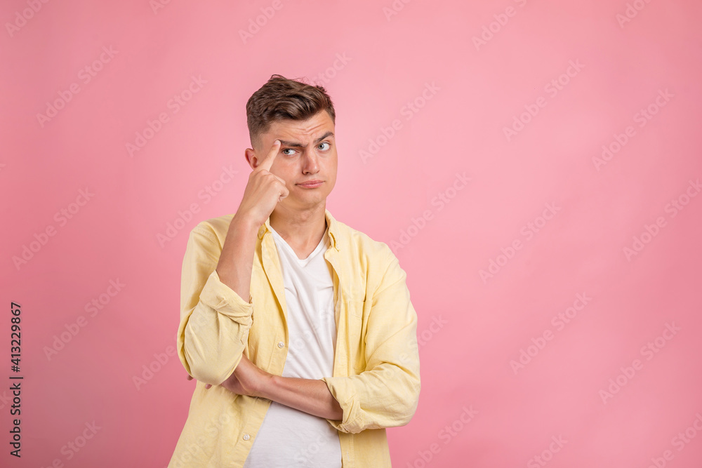 Fototapeta premium Young man thinking . Handsome man in casual clothes is pointing away, looking at camera and smiling, on pink background