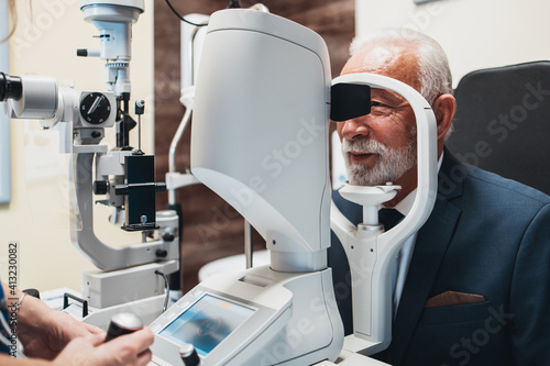 Elegant senior bearded man receiving ophthalmology treatment. Doctor ophthalmologist checking his eyesight with modern equipment.