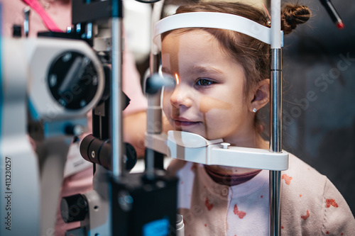 Fototapeta Naklejka Na Ścianę i Meble -  Beautiful and adorable little girl receiving ophthalmology treatment. Doctor ophthalmologist checking her eyesight with modern equipment.