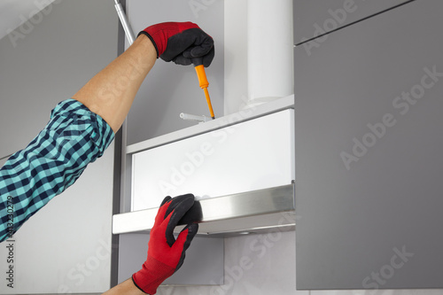 Handyman with screwdriver installs furniture in the kitchen. Worker sets a door on the gray cabinet.