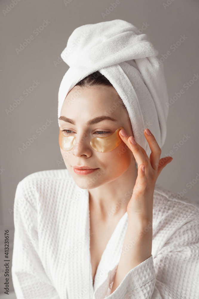 Obraz premium Pretty european girl applying golden collagen patches under her eyes. Woman facial treatment. Cosmetology, beauty and spa.