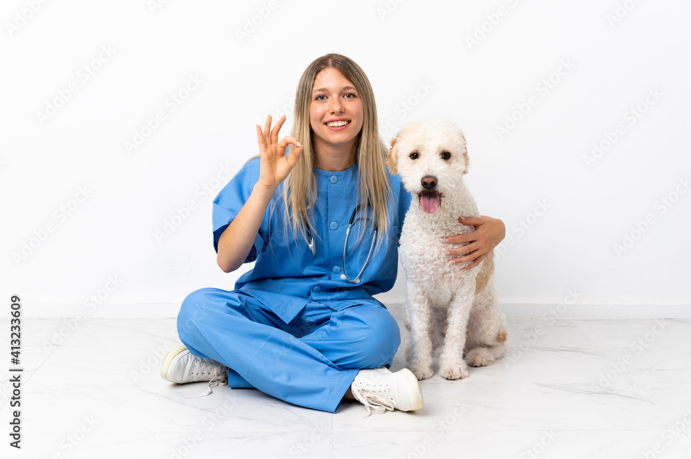 Young veterinarian woman with dog sitting on the floor showing ok sign with fingers Young veterinarian woman with dog sitting on the floor showing ok sign with fingers