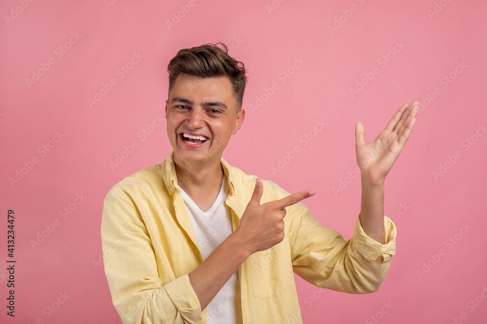 Handsome man in casual clothes is pointing away, looking at camera and smiling, on pink background Handsome man in casual clothes is pointing away, looking at camera and smiling, on pink background