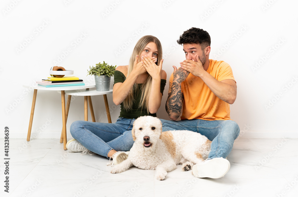Young caucasian couple with dog staying at home covering mouth with hands Young caucasian couple with dog staying at home covering mouth with hands