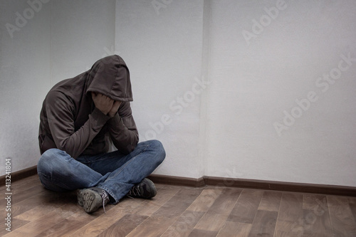 desperate young drug addict wearing hood and sitting alone in corner